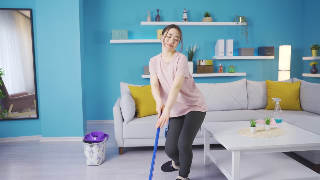 joven asiática alegre limpiando en casa divirtiéndose bailando.