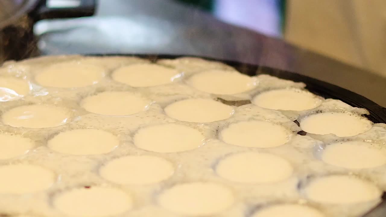 White coconut batter simmers and bubbles inside round molds of a hot cast iron pan