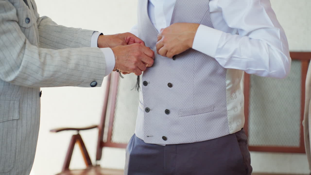 Primo piano dello sposo che sistema il gilet con aiuto mentre si prepara alla cerimonia di matrimonio