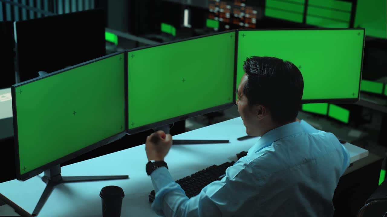 vista lateral de un hombre asiático feliz celebrando mientras trabaja con múltiples monitores de computadora simulados en la oficina