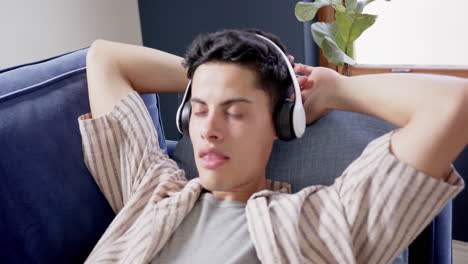 happy biracial man wearing headphones lying on couch relaxing, slow motion