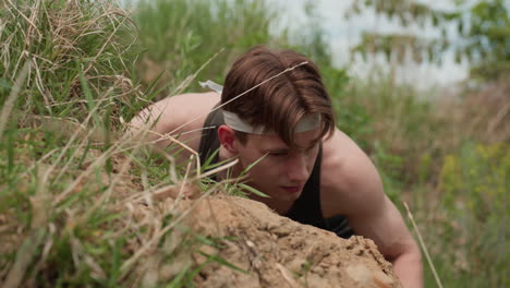 tourist lying on sandy ground with relaxed face and subtle smile, glancing forward with freckled skin and headband, surrounded by dry grass and soft hillside terrain during daylight outdoors moment