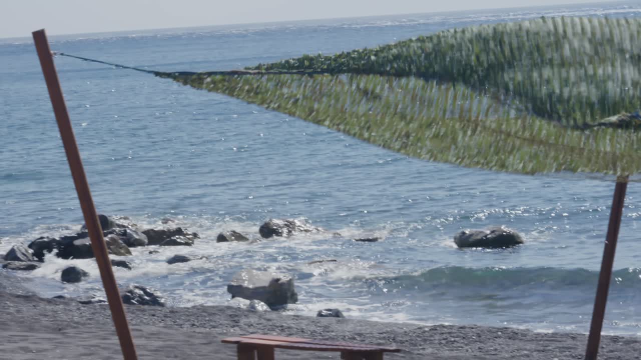 Surf board on black sand beach under shade canopy in Santorini, Greece