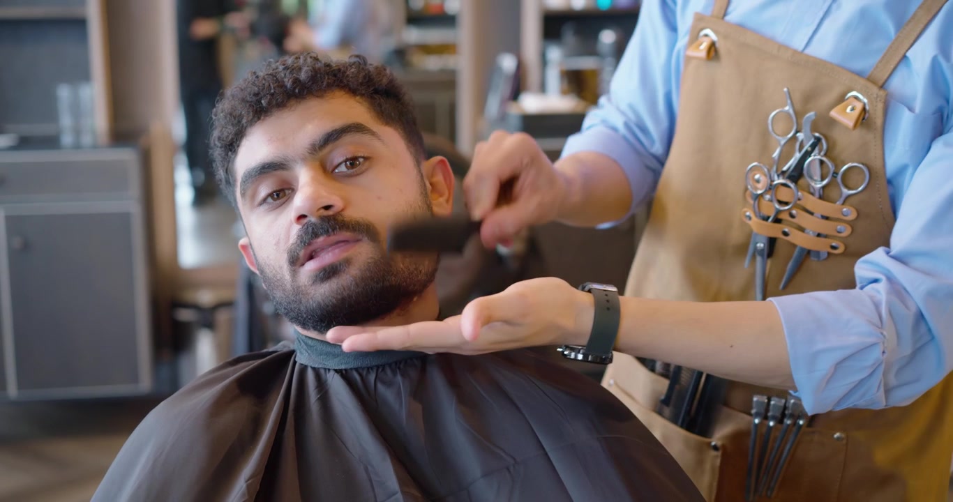 Afroamerikansk barber børster og reder kundens nakke, stikker kappen ind og former skægget i butikken.
