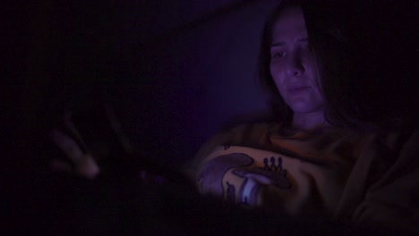 una mujer jugando con su teléfono en la cama por la noche con el reflejo de la pantalla en la cara