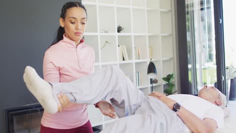 video of happy biracial female physiotherapist exercising with caucasian senior man