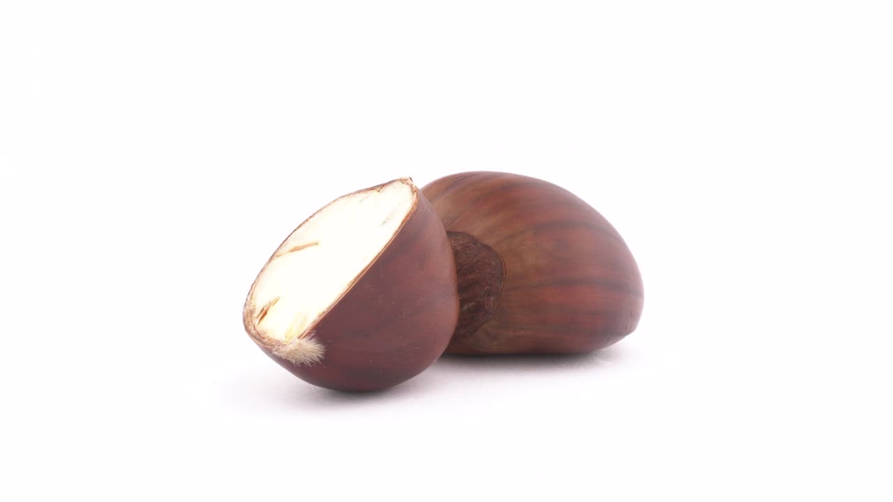 Una castagna dolce intera e una tagliata a metà. Sezione trasversale. Ruota lentamente sul piatto girevole, isolata su sfondo bianco. Primo piano. Macro.