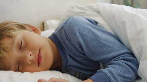 vista de cerca de un lindo niño rubio durmiendo en la cama por la mañana