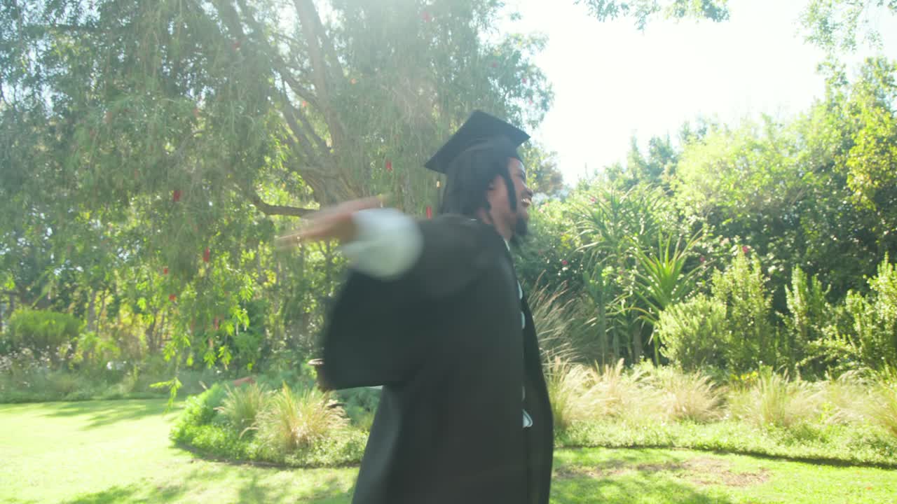 Dopo la laurea, uomo in toga nera che alza il nastro del diploma arrotolato, agita il tocco, festeggia in giardino.