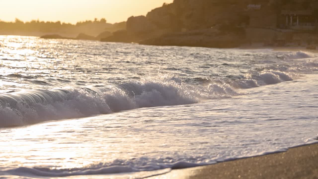 서서히 움직이는 아름다운 파도가 해가 지는 해변에 부 ⁇ 히고 있습니다.