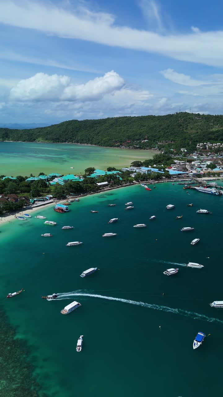 Drone slides right above Loh Dalum Beach, boats and reefs, Phi Phi Don in turquoise water