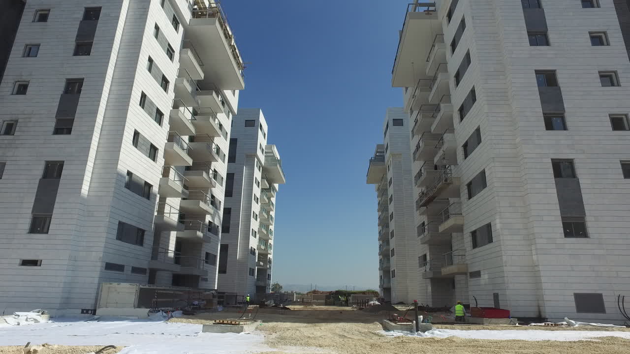 dolly adelante entre nuevos rascacielos blancos en un sitio de construcción, día soleado