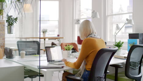 Young-business-woman-drinking-coffee-working-at-shared-workspace-desk-in-trendy-hipster-start-up-office-using-big-data-on-laptop-computer