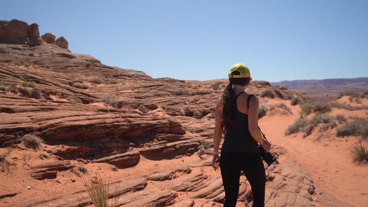 vista trasera de una mujer fotógrafa de paisajes caminando con una cámara fotográfica en el paisaje desértico de arizona, estados unidos