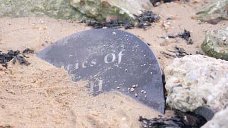 lápida de granito parcialmente enterrada en la arena de una playa