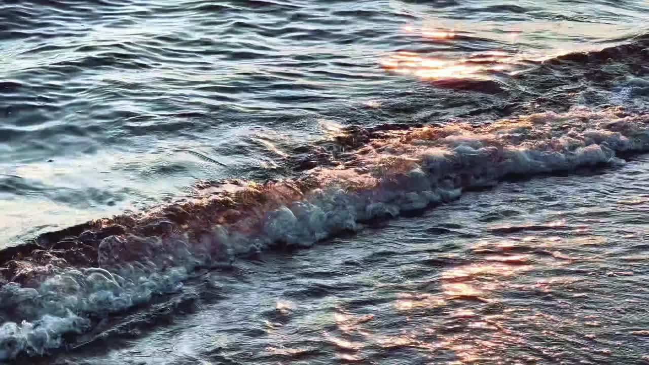 Dolci onde marine che si infrangono sulla riva al tramonto con riflessi dorati della luce solare.