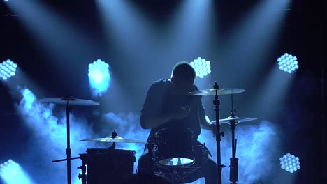 silhouette drummer playing on drum kit on stage in a dark studio with smoke and neon lighting. dynamic neon lighting effects. performance vocal and musical band. close-up