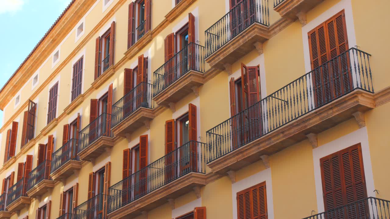 An elegant building featuring traditional balconies, illuminated by warm sunlight. The vibrant colors enhance the charming atmosphere of the urban landscape.
