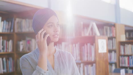 asian female student wearing a blue hijab standing and talking on a smartphone