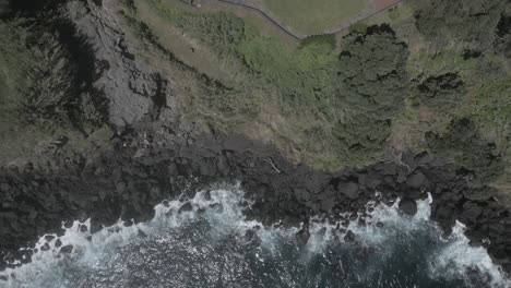 Waves-crashing-against-rugged-coastline.-Aerial-top-down-ascending