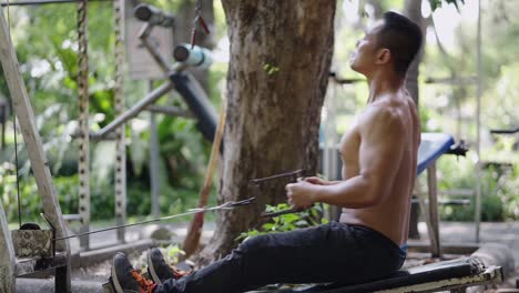 shirtless man doing cable rows at an outdoor gym