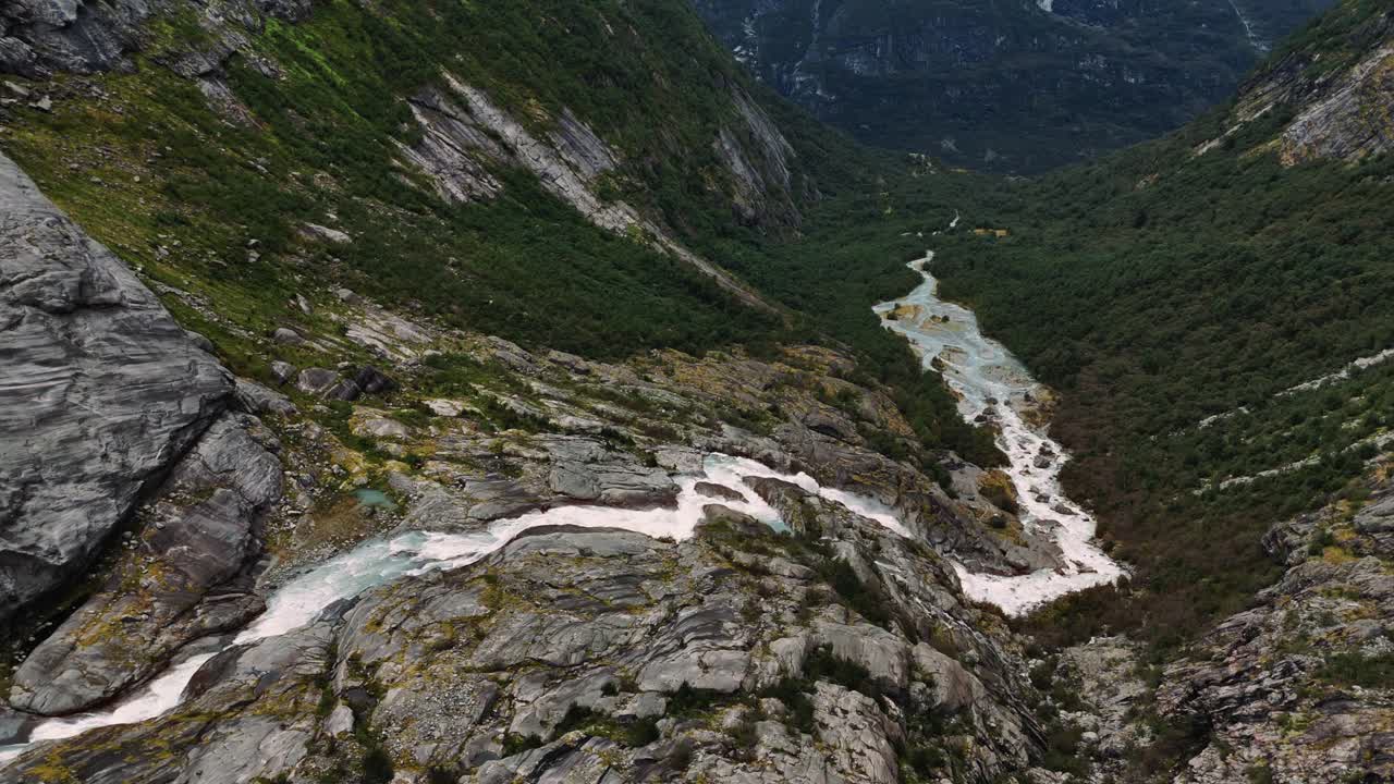 Spettacolare cascata che scende su rocce coperte di muschio in una ripida valle con pendii verdi, Norvegia, drone.
