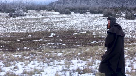 a close up shot of a traditional bushman walking through a snowy mountain landscape