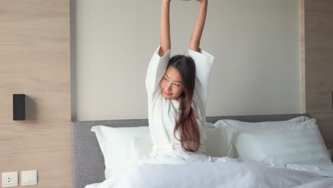 atractiva mujer asiática estirándose en la cama en una hermosa mañana después de un buen sueño, toma estática con espacio para copiar