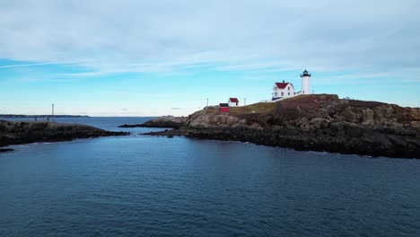 Close-angle-over-water-of-a-lighthouse-on-a-rocky-island-with-coastal-tides-crashing-on-the-shoreline