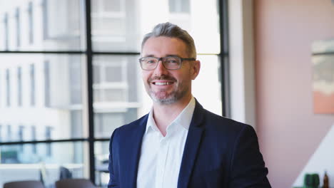 Portrait-Of-Smiling-Mature-Businessman-Wearing-Glasses--Standing-In-Empty-Office