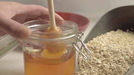 hand stirring pot of golden runny honey with scoop of oats