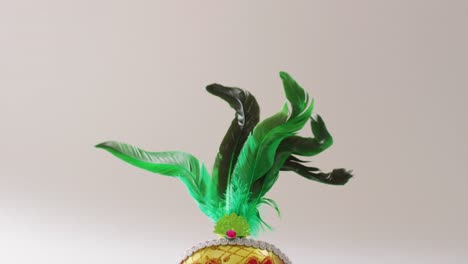 video of red and gold masquerade mask with green feathers on white background with copy space