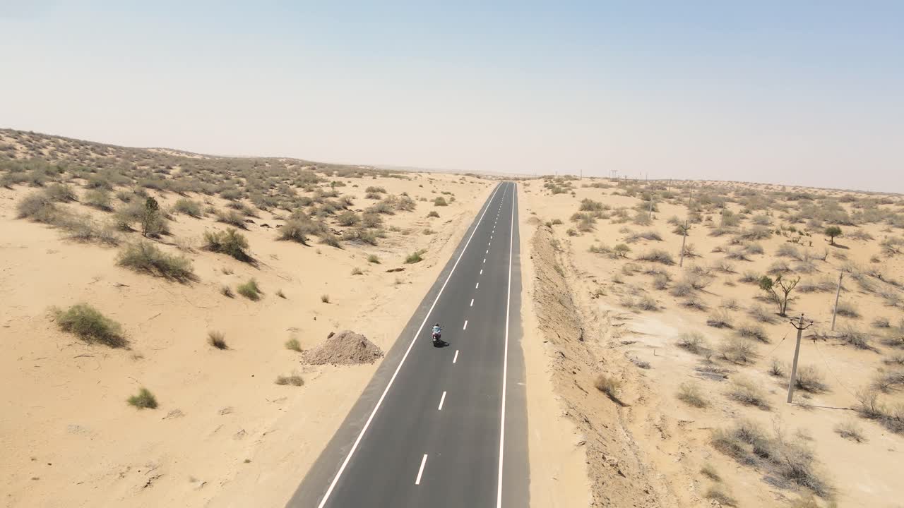 Aerial drone shot tracking a motorcyclist cutting through desert terrain with dust trailing behind.