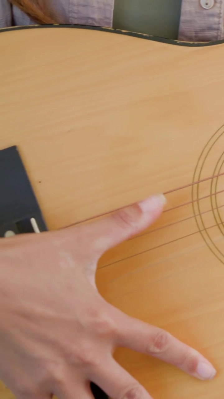 Vertical video: Strumming woman in beige top playing at home, hand touching acoustic guitar strings