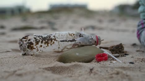 nahaufnahme eines babys, das eine plastikflaschenkappe am strand aufnimmt