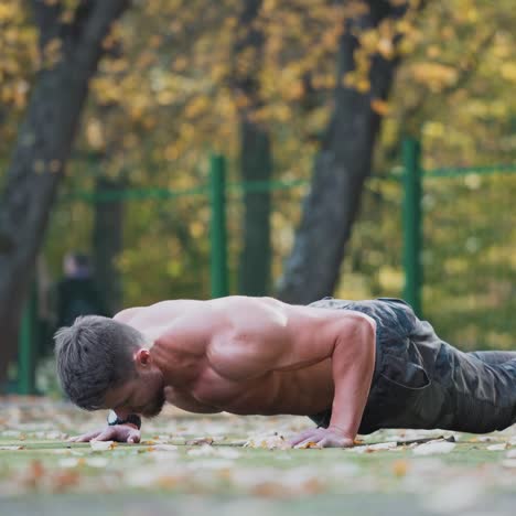 muscular athlete doing push-ups outside. sporty guy is training in nature. bearded male athlete exercising push-up on the stadium in autumn. healthy lifestyle concept.