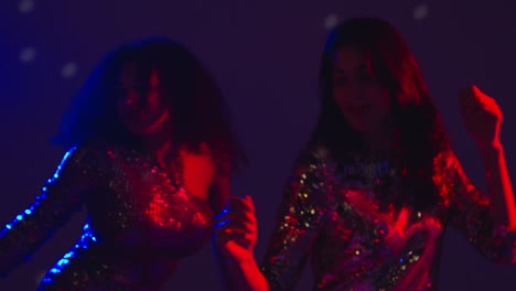 close up of two women in nightclub bar or disco dancing with reflected sparkling lights