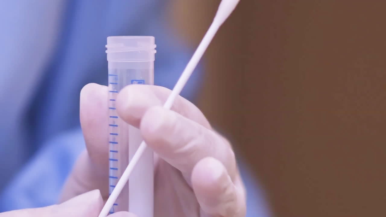 Doctor places a COVID-19 test swab into a swab tube, extreme close up shot.