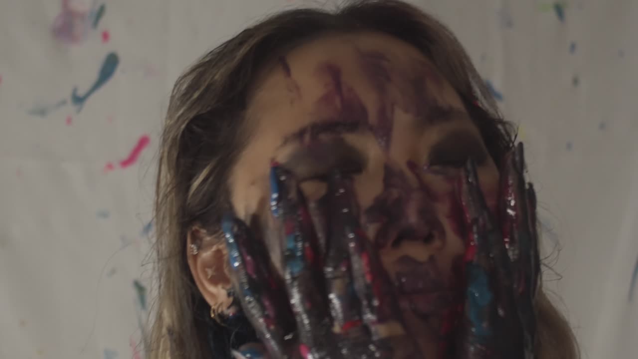 Asian woman with colorful paint on face and hands, moving hands on face and body, gesturing
