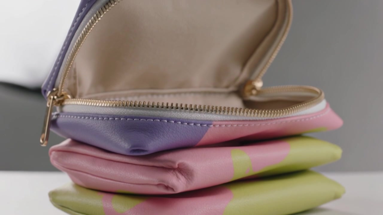 Tirando la cerniera dorata, la pochette superiore di tre pochette pastello si apre su un tavolo bianco, mostrando la fodera beige