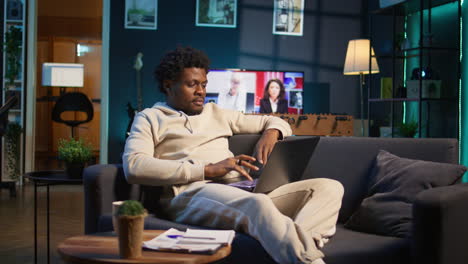 black man does his research by reading articles and taking notes at home, collecting information for a new project. freelancer multitasking and studying files with data driven papers. camera b.