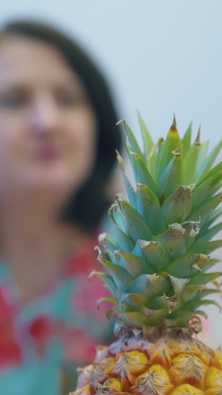 yellow pineapple green top against blurred woman with short dark hair enjoying eating fruits extreme close view