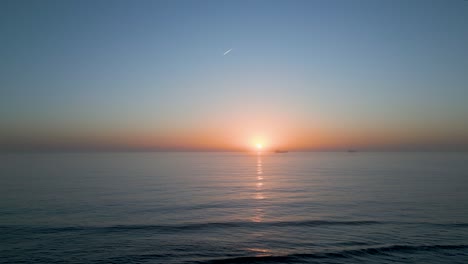 Drohne-Fliegt-über-Die-Küstenstraße-Mit-Einem-Fantastischen-Blick-Auf-Die-Küste-Von-Cascais-Mit-Einem-Roten-Und-Orangefarbenen-Himmel-Zur-Goldenen-Stunde-Mit-Einigen-Segelbooten,-Portugal