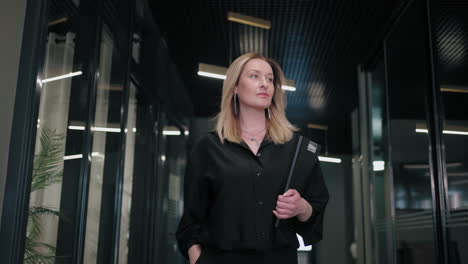 a happy blonde business woman of 30-40 years in a black shirt walks down the corridor of the business center carrying documents