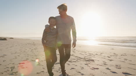 father with arm around son walking along winter beach