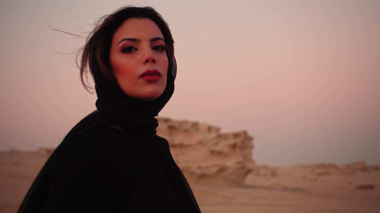 niña mirando directamente a la cámara con ojos inocentes sosteniendo una bufanda negra en sus manos volando hacia la cámara para cubrir la lente en las dunas fósiles uae dubai abu dhabi