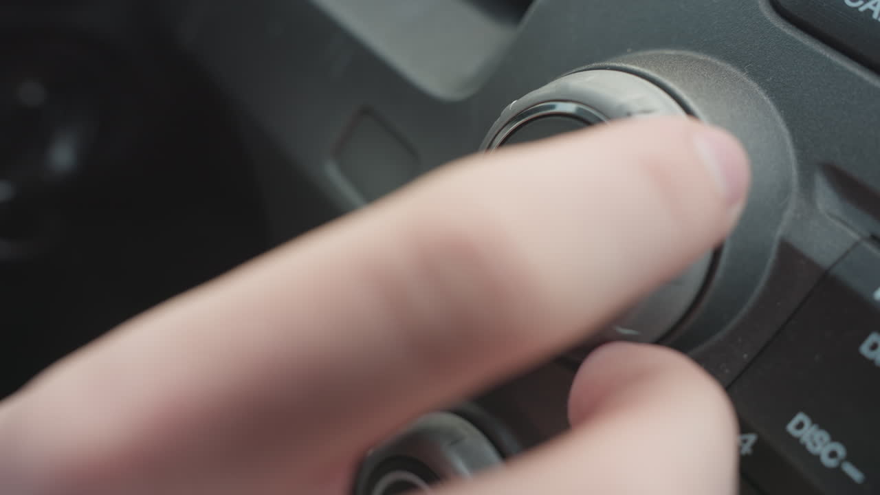 Close up of hand pressing volume push power knob then rotating dial to adjust audio settings on car stereo control panel capturing finger interaction with vehicle interior media interface