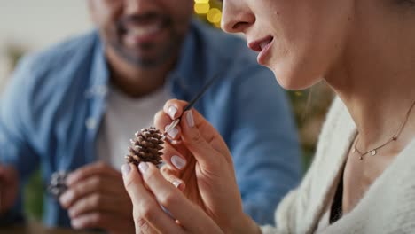 Multi-ethnicity-couple-decorating-cone-with-white-paint-during-Christmas-time-at-home.