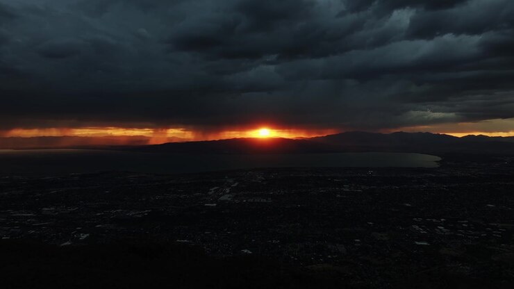 Wide aerial trucking right drone shot of Utah Valley during a vibrant orange fall sunset from Khyv Peak near Provo, Utah on a stormy evening in October