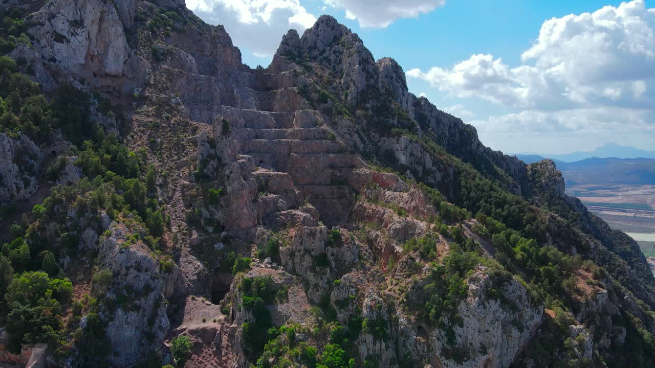 A breathtaking aerial view of rugged cliffs and ancient ruins, nestled amidst lush greenery and dramatic rock formations in Tunisia's Jbal Ressas.